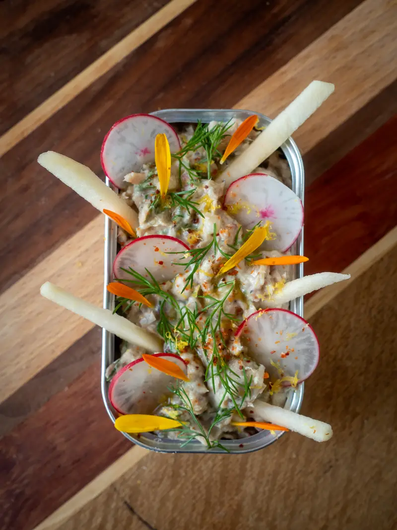 Close-up van rilettes van sardines in een blikje, gegarneerd met verse dille en appelstaafjes